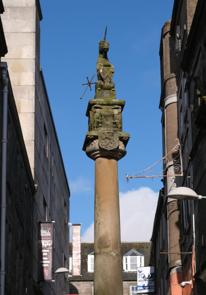 Stone Mercat cross topped by unicorn and blue sky background.